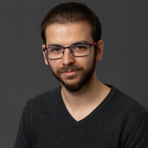 Headshot of André, a white man with short hair, glasses and a full short beard. He is staring directly at the camera with a closed-mouth smile and wearing a black long-sleeve shirt.