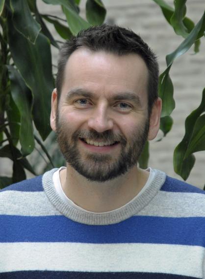 A portrait of David Flatla, a smiling white male with brown hair and short brown beard, wearing a blue and grey sweater.
