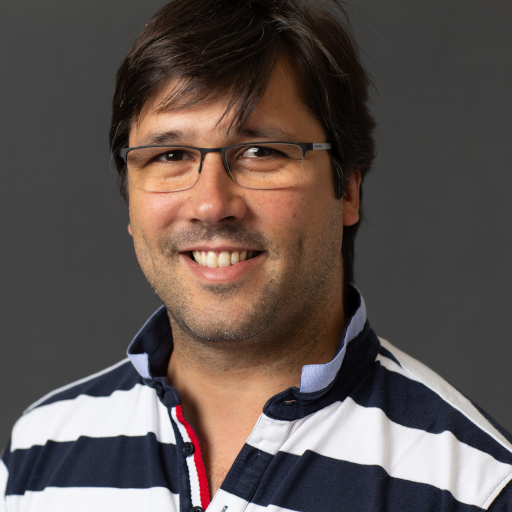 Headshot of Tiago Guerreiro, a browned-hair man wearing glasses and a blue and white horizontal stripes polo shirt.