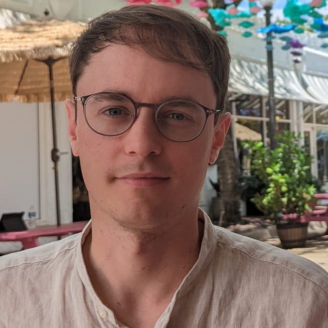 Headshot of Timothy Neate, a white, brown-haired male in glasses, wearing a white shirt with colourful Miami scene in the background.